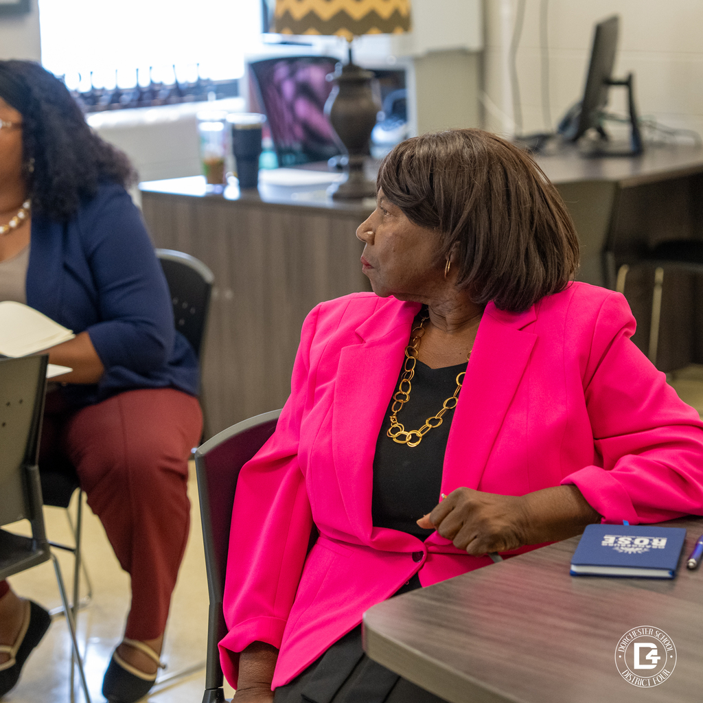 Community member in a bright pink blazer seated during the mentoring program orientation.