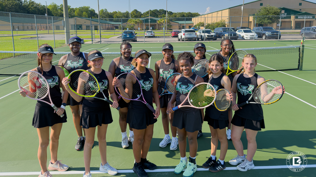 Woodland ladies tennis team posing on the court holding rackets. Ladies are positioned in two rows wearing match black uniforms with the woodland logo on the front.