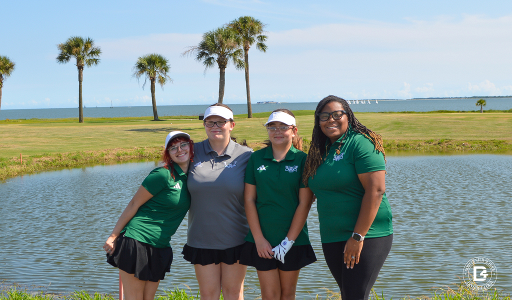 Woodland High School girls golf team and coach pose together beside a pond on the golf course.