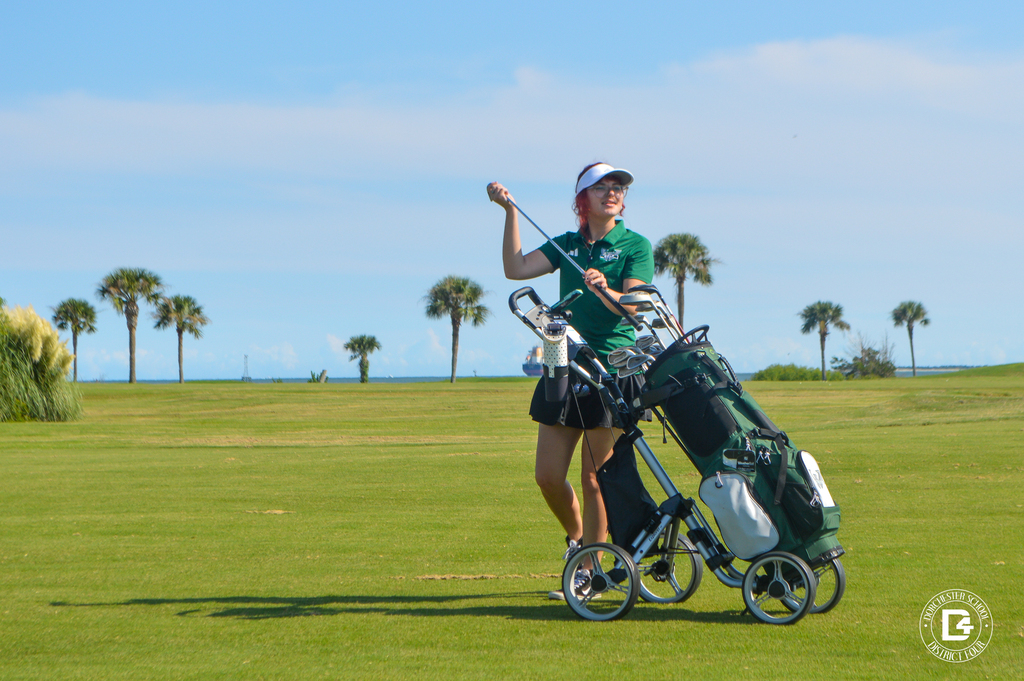 Woodland High School golfer stands beside her golf bag while holding a club.