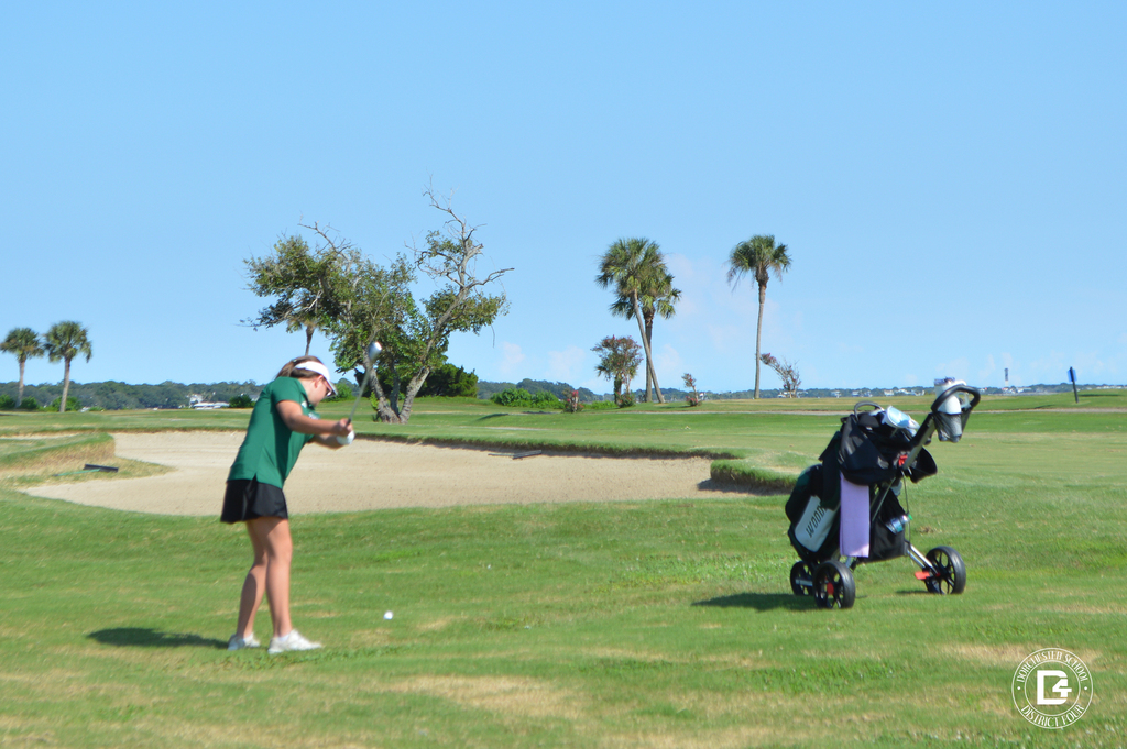 Woodland High School golfer swings a club on the course near a sand bunker.