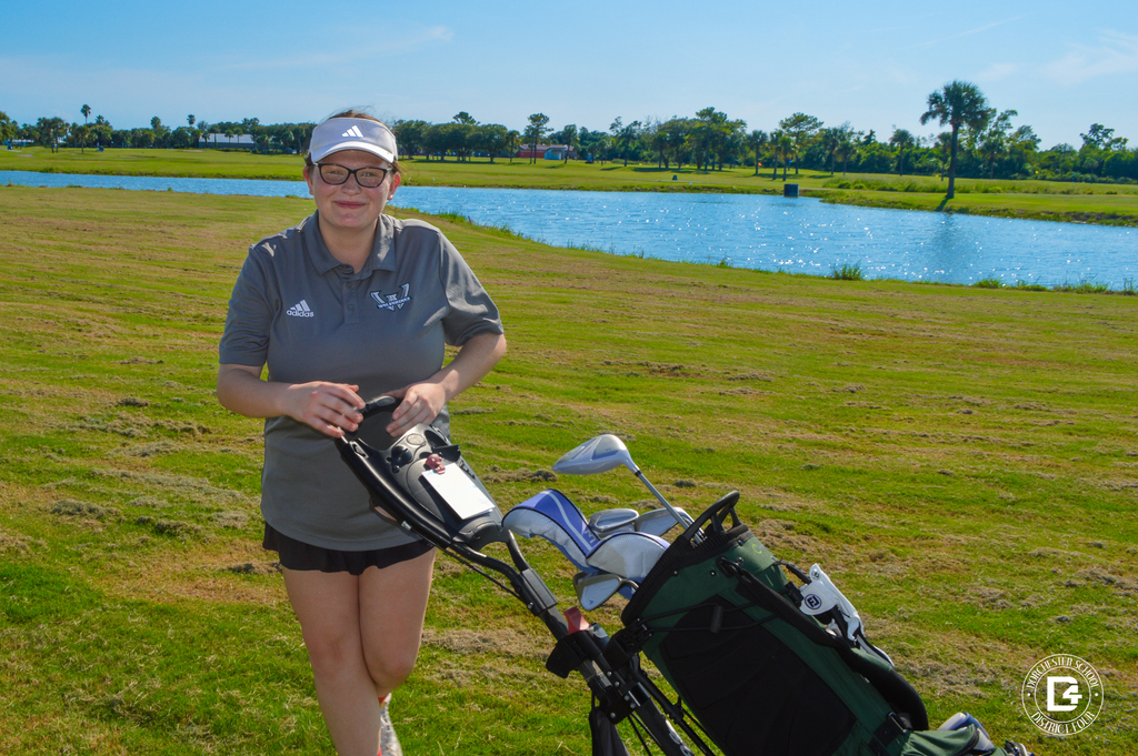 Woodland High School golfer poses beside her golf bag near a pond.