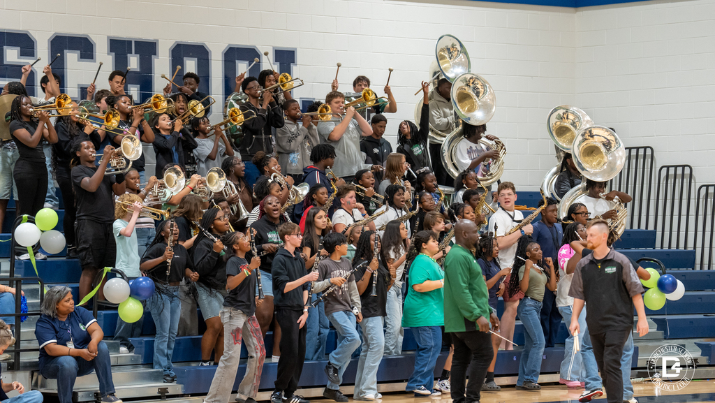 The Marching Wolverines from Woodland High School perform in the stands, playing trumpets, trombones, clarinets, saxophones, and sousaphones with balloon decorations nearby.