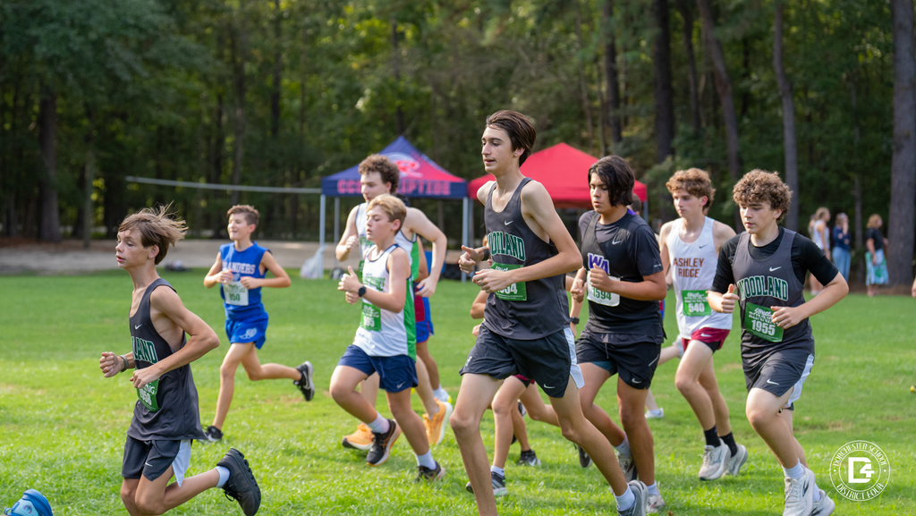 A pack of boys runners, including Woodland High School athletes wearing bibs 1958 and 1955, moves across the grass at Wannamaker Park with team tents and trees in the background.