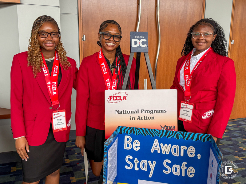 Three Woodland High School FCCLA students wearing official red blazers stand beside their National Programs in Action STAR Events display titled Be Aware, Stay Safe during the FCCLA National Leadership Conference in Washington, D.C.