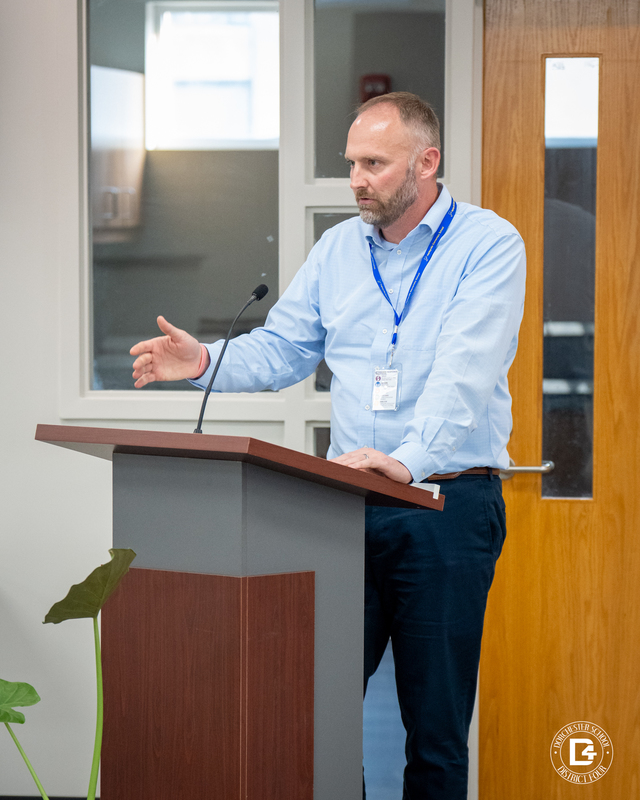 Jeremy Wolfgang, Harleyville Elementary Principal. A man in a light blue shirt and navy slacks speaks at a podium with a microphone, addressing the board with a hand gesture.