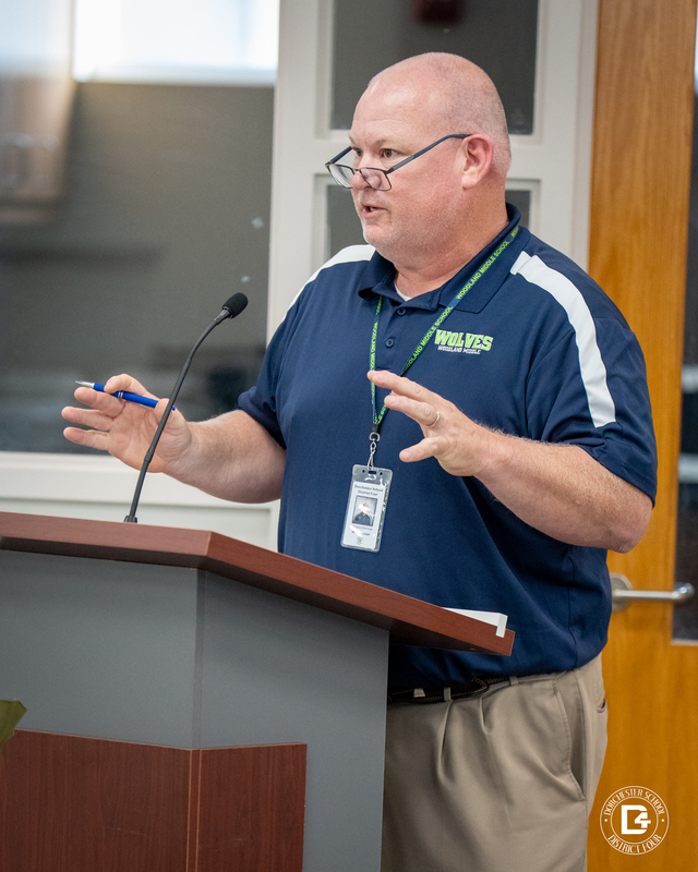 Benji Kennedy, Woodland A man in a navy Woodland Wolves polo shirt gestures with his hands while speaking at a podium during the meeting. Middle School Principal 