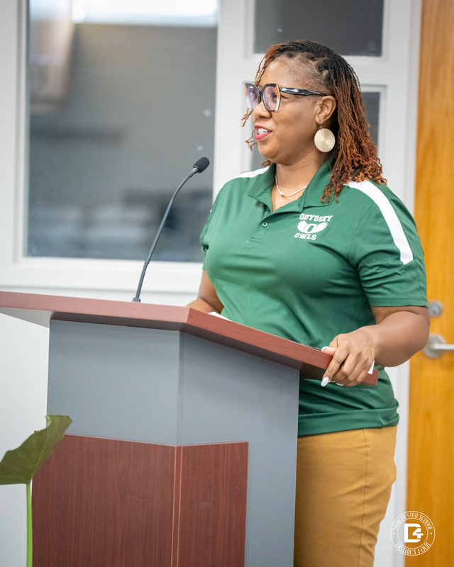 Tamara Boyd, Odyssey Educational Center Counselor.  A woman wearing a green Odyssey Owls polo shirt and glasses speaks at a podium with a microphone during the board meeting.