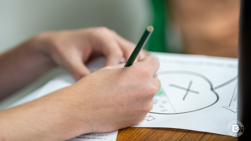 A close-up of hands holding a pencil while labeling a photosynthesis worksheet with arrows and diagrams.