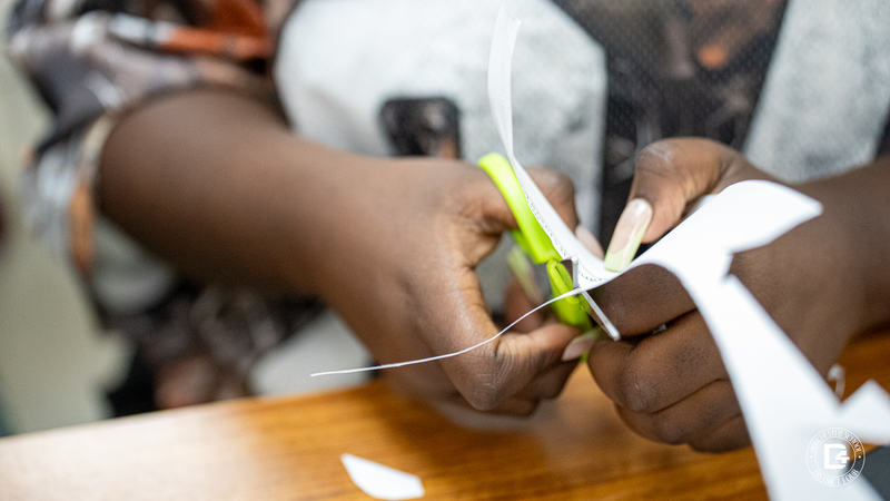 Close-up of a student’s hands using green scissors to cut out a piece of paper for the photosynthesis project.
