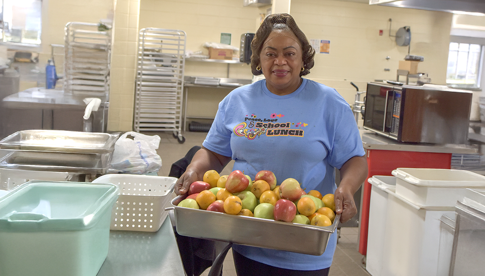 A lunch lady holding a container of apples