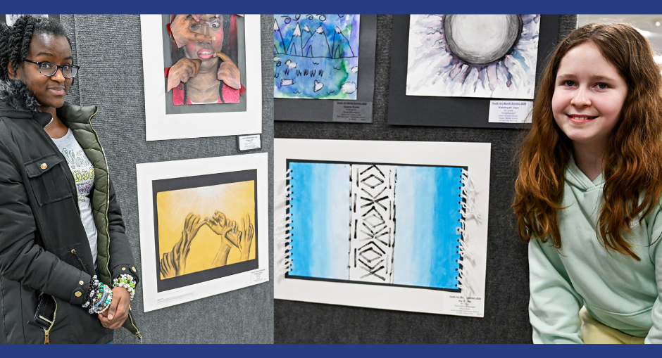 Two students stand next to their art during the 2026 Art Show at the central office.