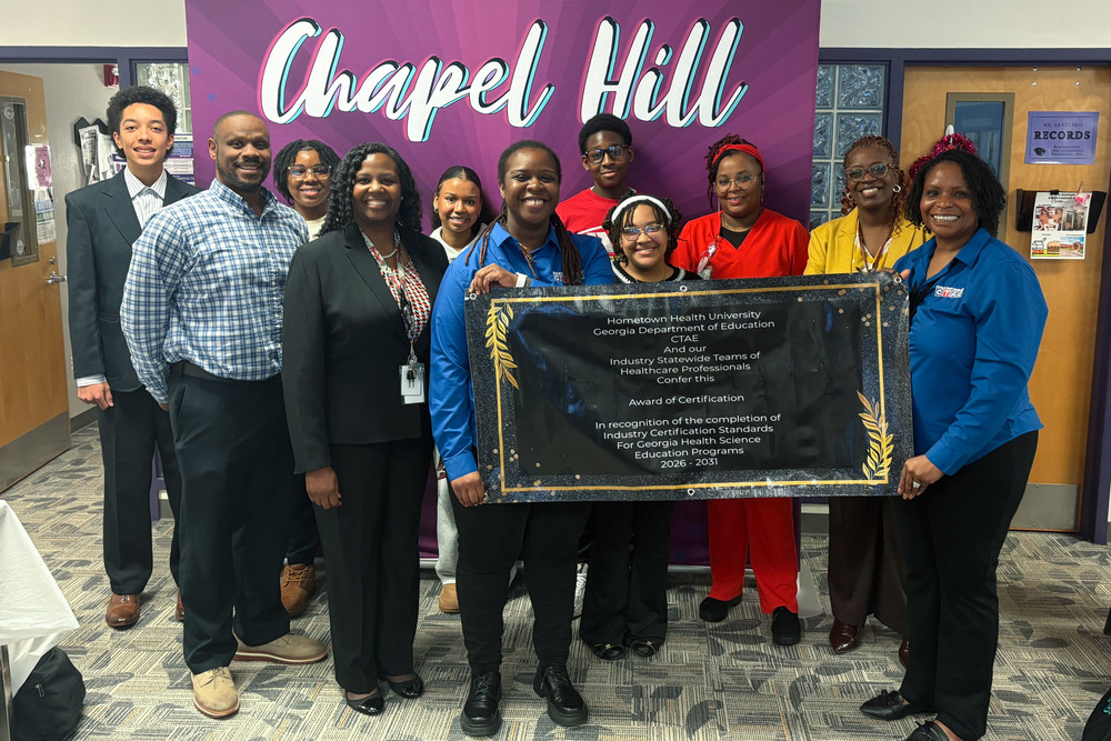 Chapel Hill High students and staff and DCSS Executive Director of CTAE Tekmekia Gilchrist hold up their Industry Re-Certification in Healthcare banner.
