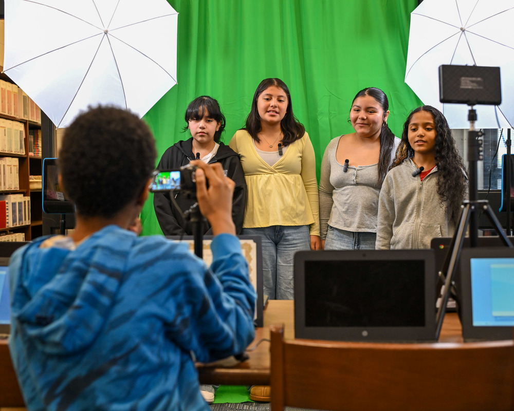 Stewart students stand in front of a green screen with studio lights while another student makes a video of them reading a study guide.