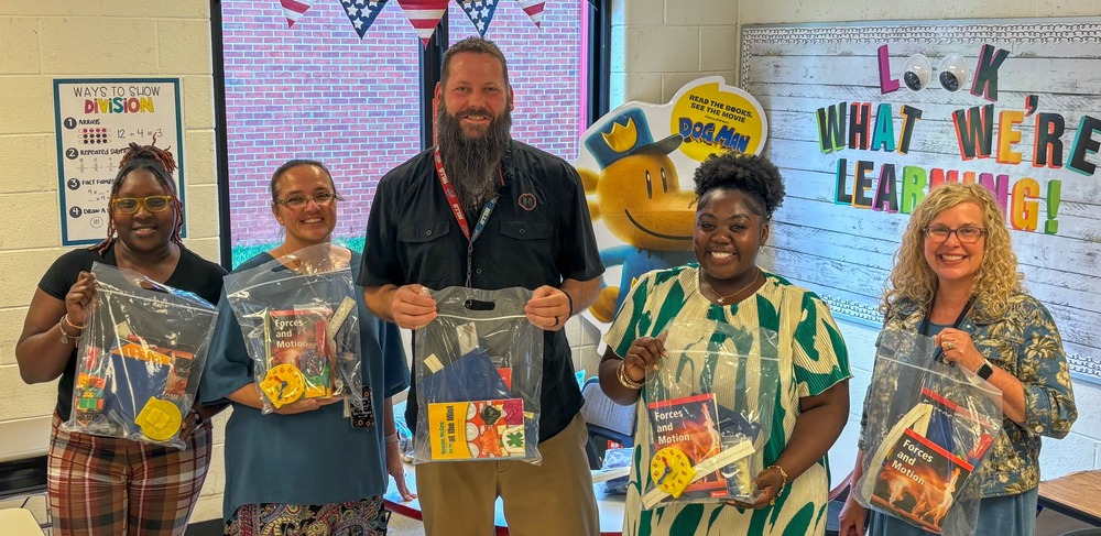 MLES third grade teachers hold up resource bags distributed to students.
