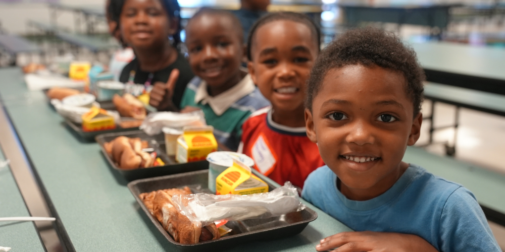 Students smile with their lunch tray during Kinder Camp in 2026.
