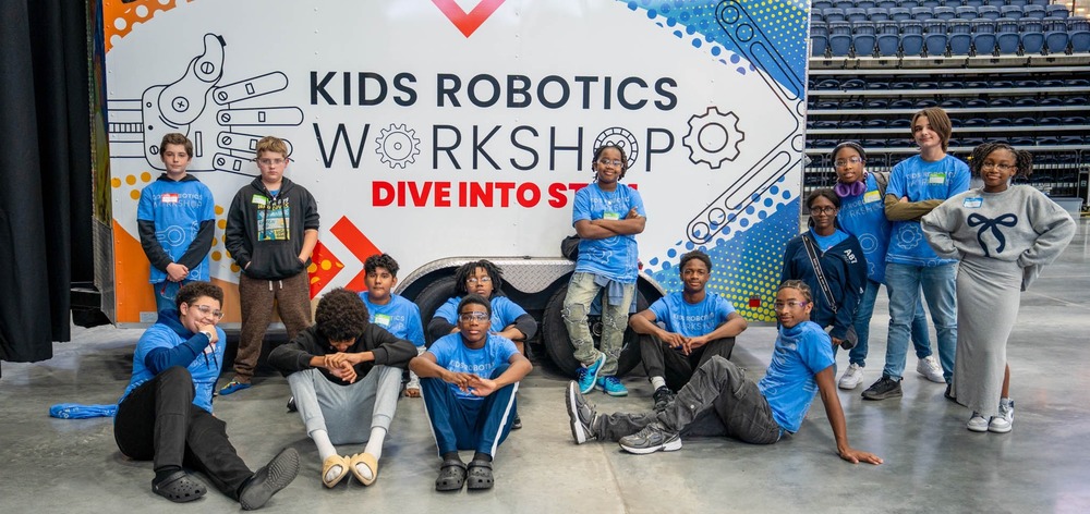 Students in front of a Kids Robotics Workshop backdrop at Legacy Arena.