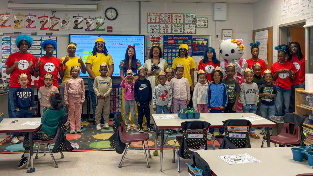 Group photo showing adults dressed in costumes and students with paper crown hats.