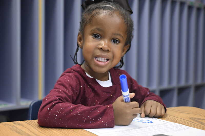 A little boy colors with a blue marker during Kinder Camp.