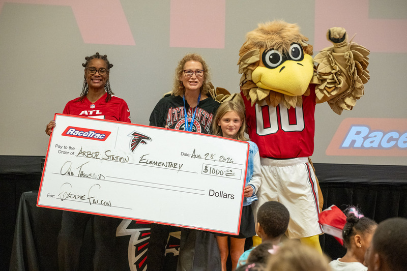 Arbor Station Principal Anitra Paige, staff member and student hold up the $1,000 check from the Falcons with Freddie Falcon.