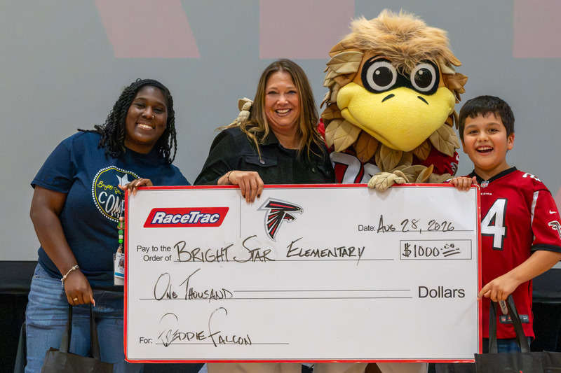 Bright Star Principal Heather Fields, staff member and student hold up the $1,000 check from the Falcons with Freddie Falcon.