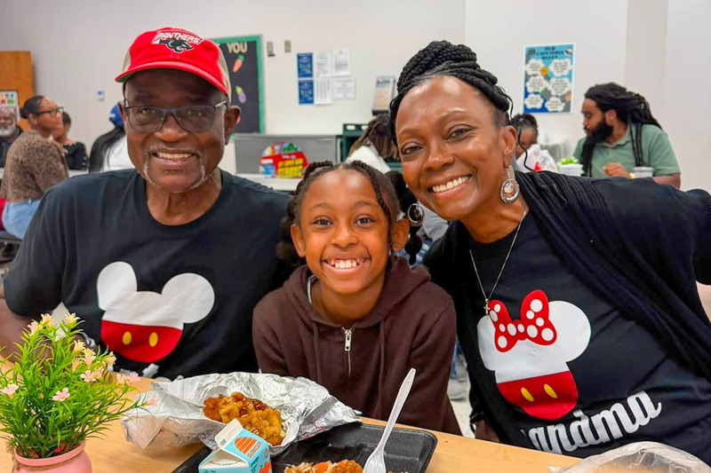 Grandparents wearing Disney shirts smile with their granddaughter.