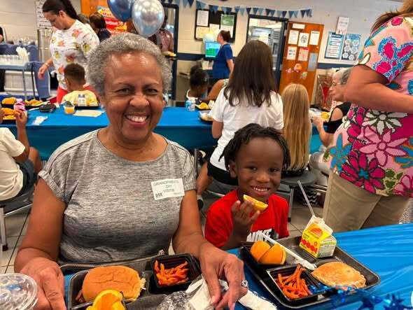 A grandmother and her grandson smile while eating lunch.
