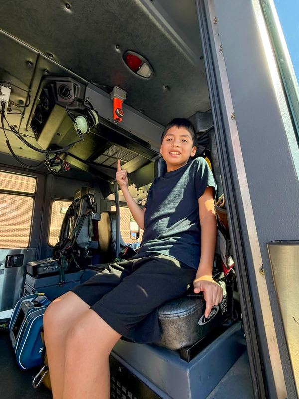 A Mason Creek student points up while sitting in a fire truck at a special event with first responders.