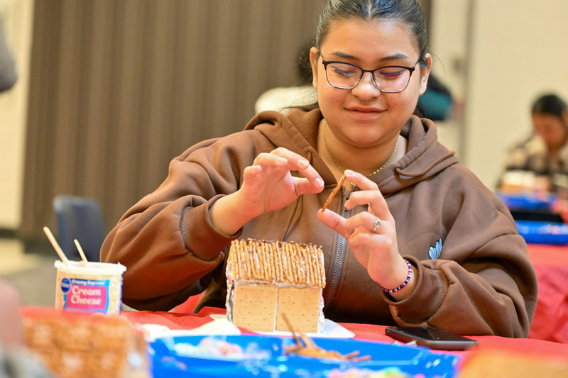 A Newcomer Center student adds a pretzel stick to the roof of her gingerbread house.