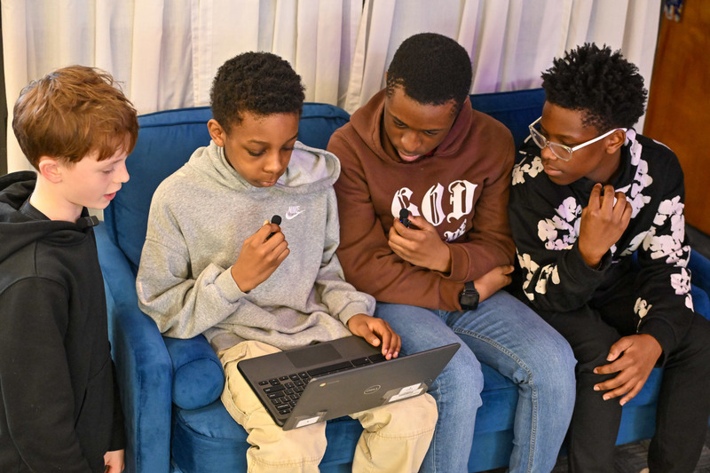 Stewart students speak into microphones while one holds a laptop to record a podcast.