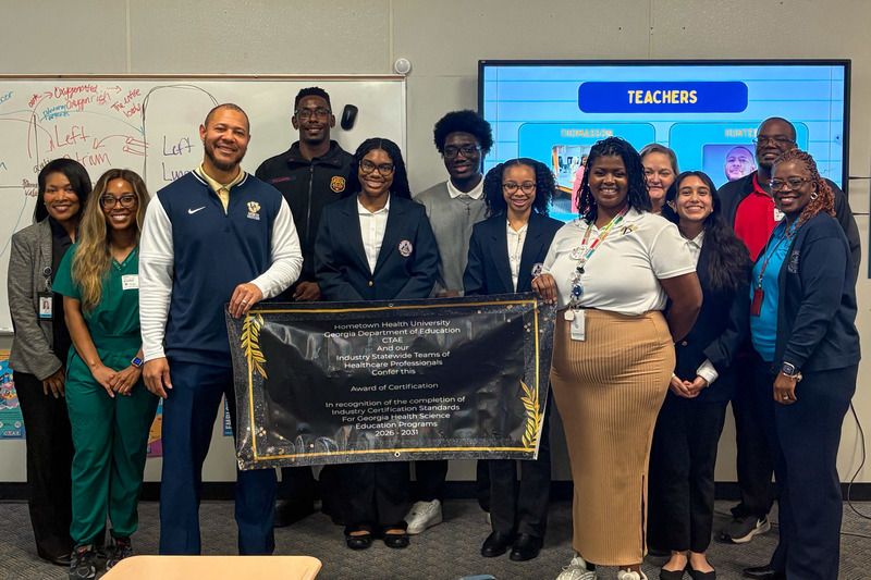 Douglas County High students and staff and Tekmekia Gilchrist hold up their Re-Certification in Healthcare banner.