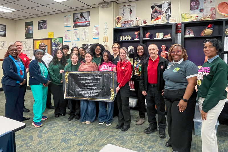 Lithia Springs High School students and staff and Tekmekia Gilchrist hold up their Re-Certification in Healthcare banner.
