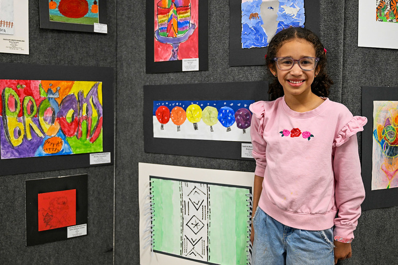 A student stands next to her painting at the Youth Art Show.