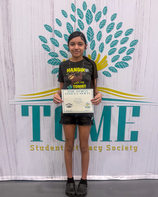 A student holds up her certificate in front of the TomeCon backdrop.