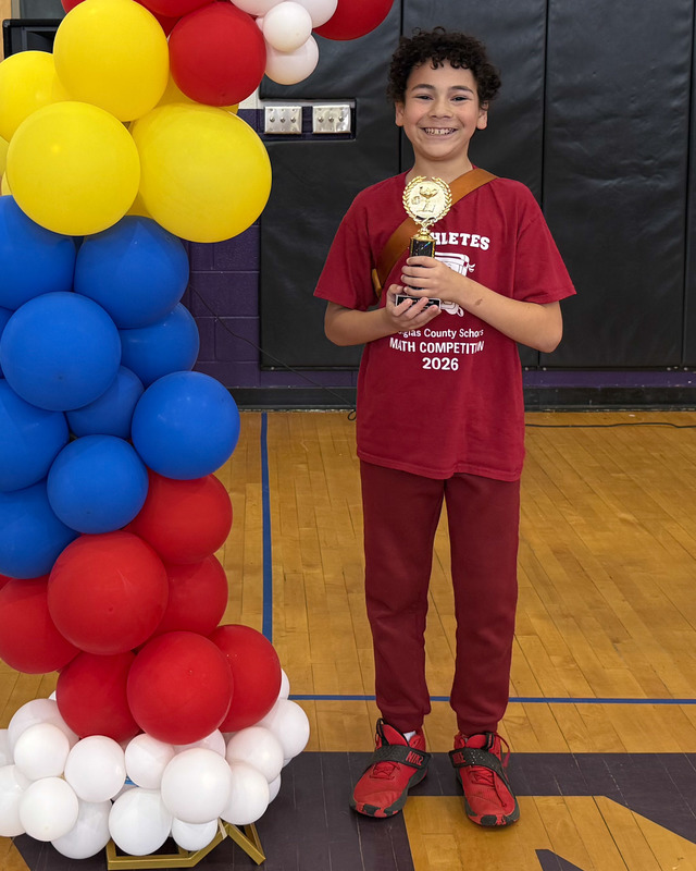 An elementary student holds up his first place trophy in the math competition.