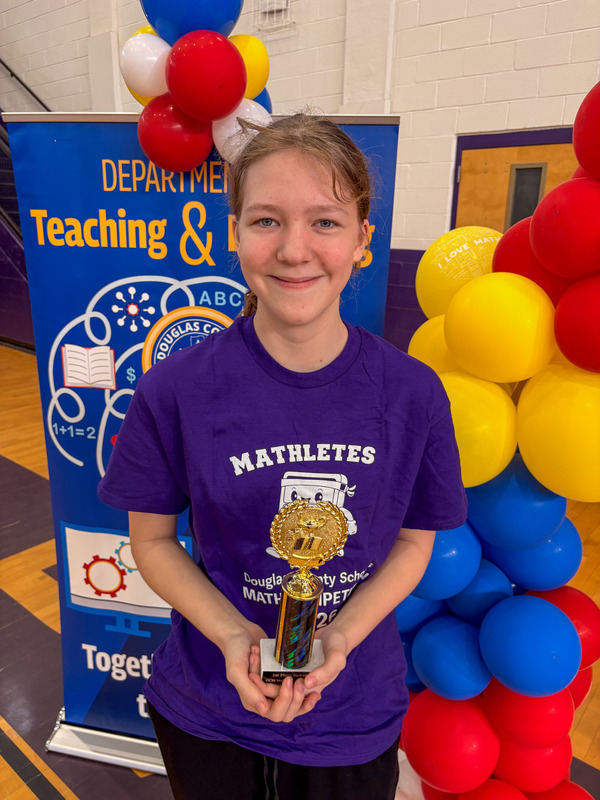 A middle school student holds up their trophy for winning the math competition.