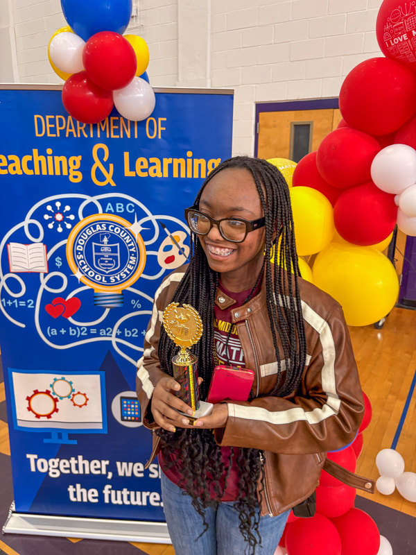A middle school student holds up their trophy for winning the math competition.