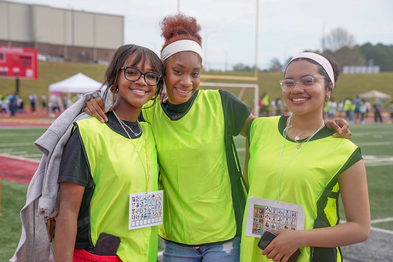 Three high school volunteers wearing green vests are pictured during the Special Olympics.