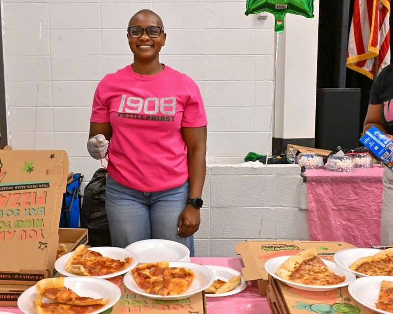 An Alpha Kapp Alpha Sorority member smiles while serving pizza to Eastside students.