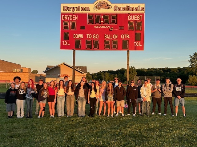 group of high school seniors standing in front of a football scoreboard