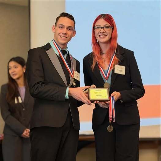 photo of two high school students holding an award plaque and medals