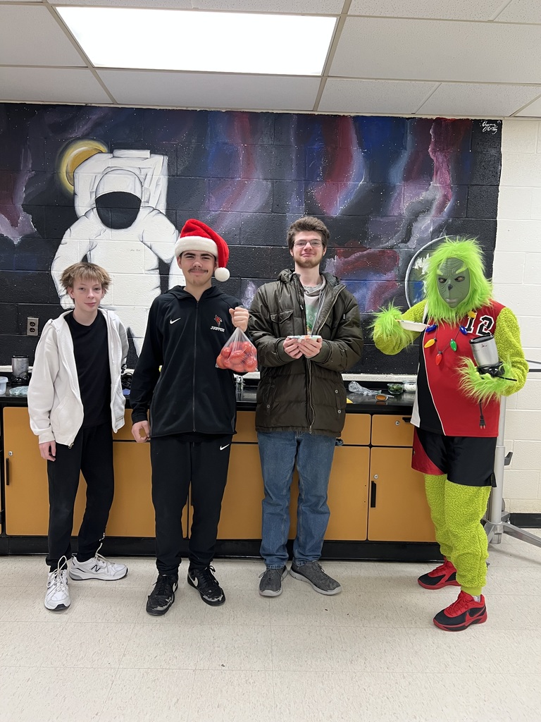 three high school boys standing next to a person in a grinch costume