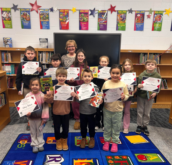 Students and an adult in a school, holding up certificates.