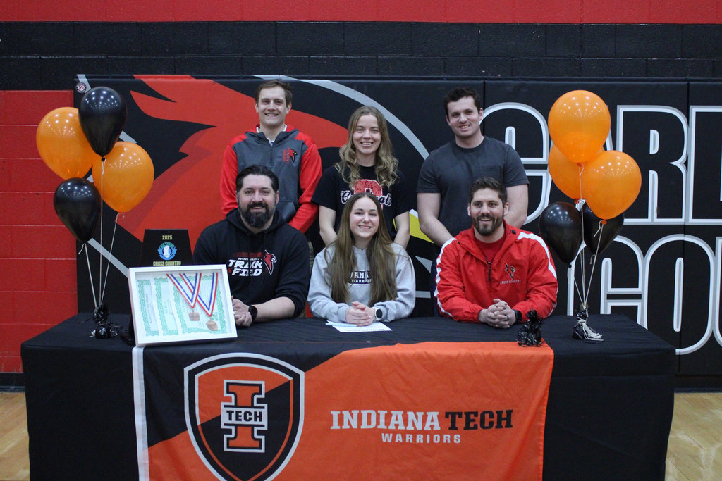 high school athlete sitting behind a table with five coaches
