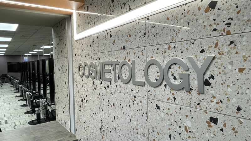 A view of the new cosmetology school, looking from the front reception desk back into the salon area where a long row of empty seats are lined up at stations where students will learn and practice cosmetology.