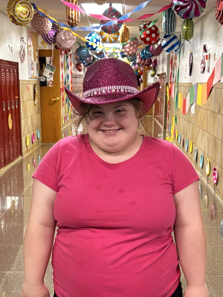 student stands smiling dressed in pink in decorated hallway