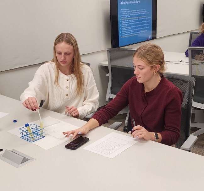 2 students practicing a mock urinalysis