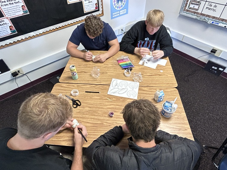 4 male students work on decorating their calavera
