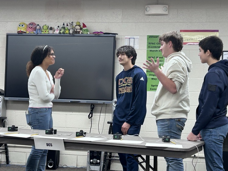 a girl student looks towards her 3 male teammates as they dicsuss a bonus question