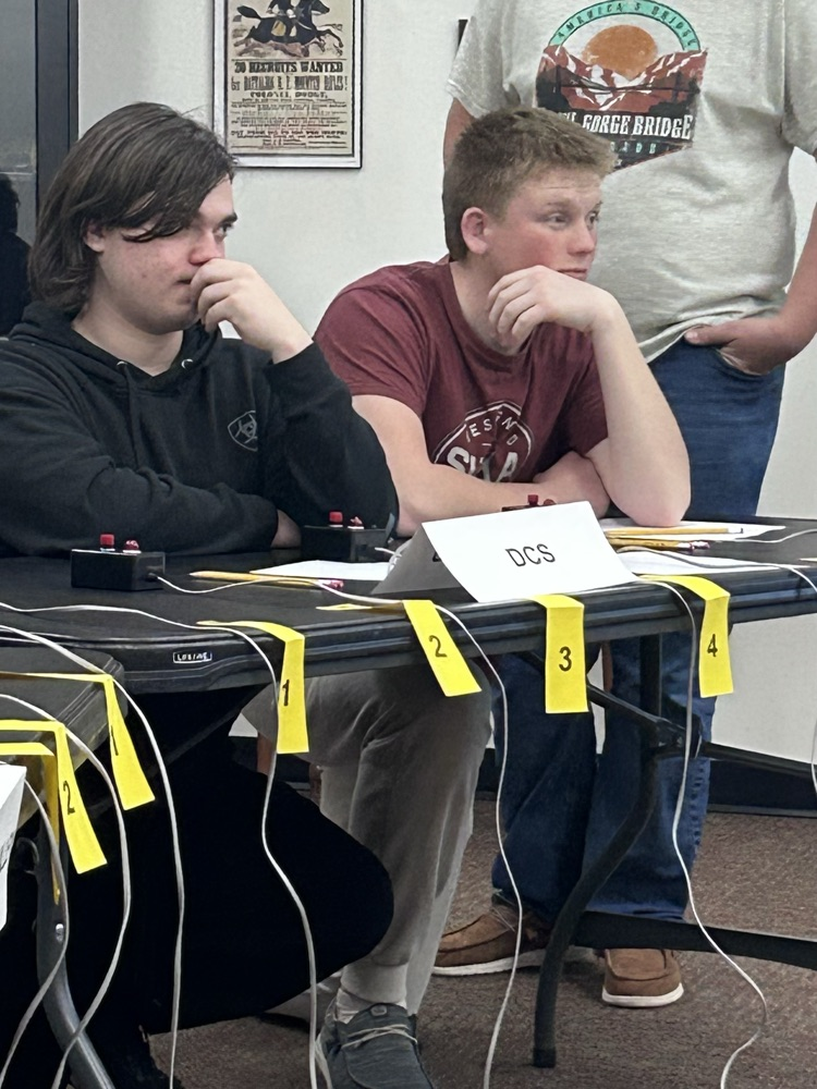 Team captain Noah and team member Jack kneel behind a table with fingers hovering over their buzzers